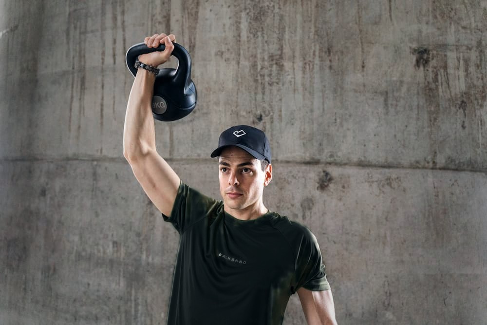 Jared, founder and head coach, pressing a kettlebell overhead against a concrete wall
